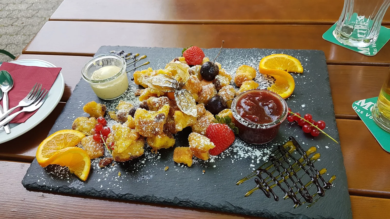 Kaiserschmarrn mit Beeren, Orangenspalten und zwei Schälchen auf einer Schieferplatte im Gastgarten