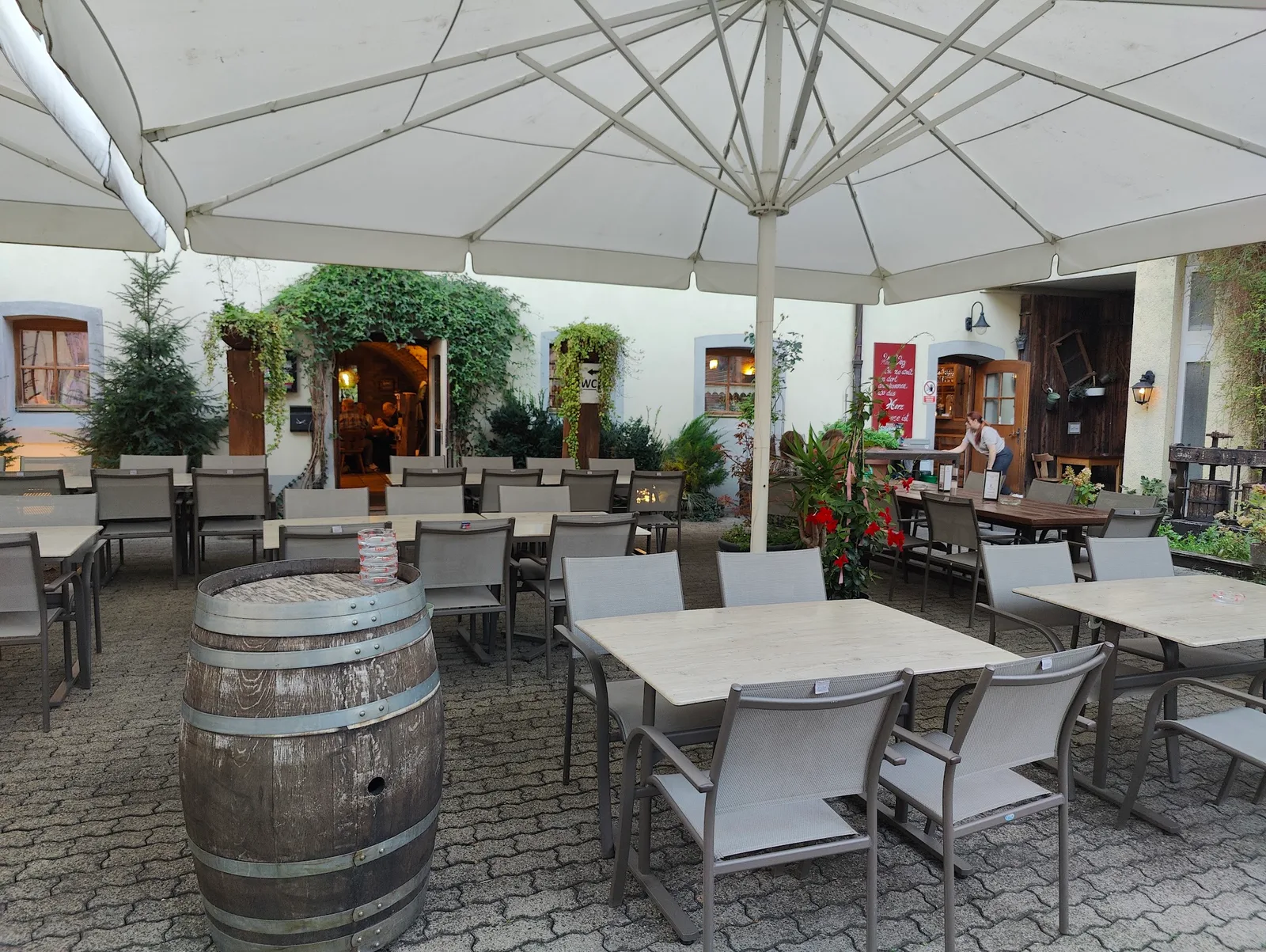 Der Gastgarten mit Sonnenschirmen, einem alten Weinfass und dem Eingang zum Keller