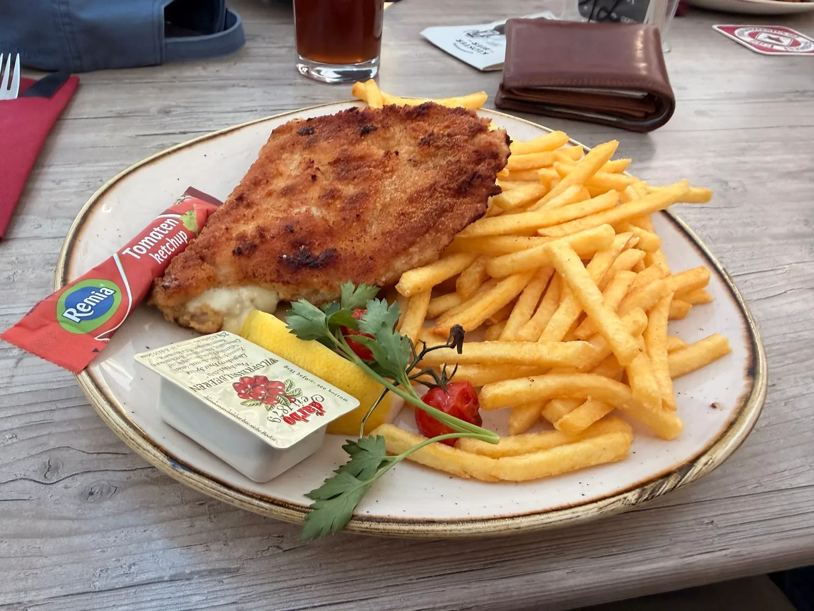 Cordon bleu mit Pommes frites, Zitrone und Preiselbeeren auf einem Tisch im Gastgarten